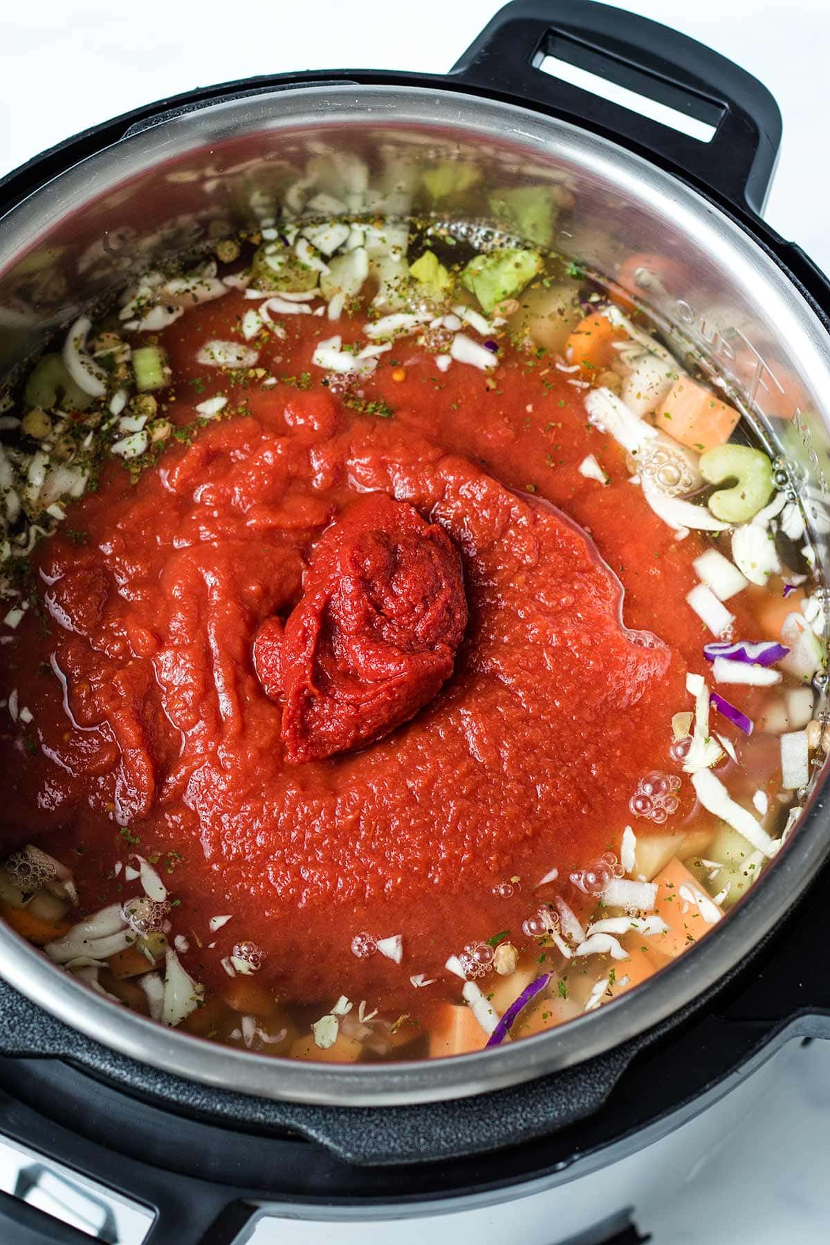 Crushed tomatoes and tomato paste layered on top of vegetables, lentils and broth in an Instant Pot.