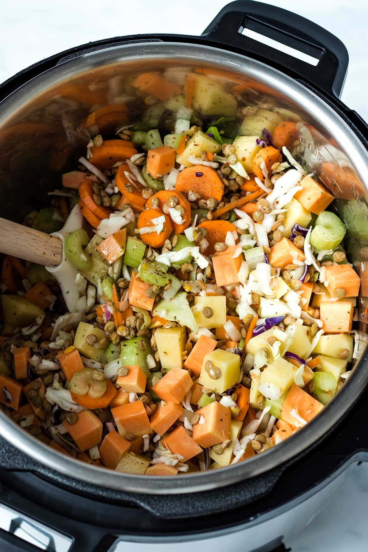 Lentils, vegetables and seasoning mixed together with a spatula in an Instant Pot.