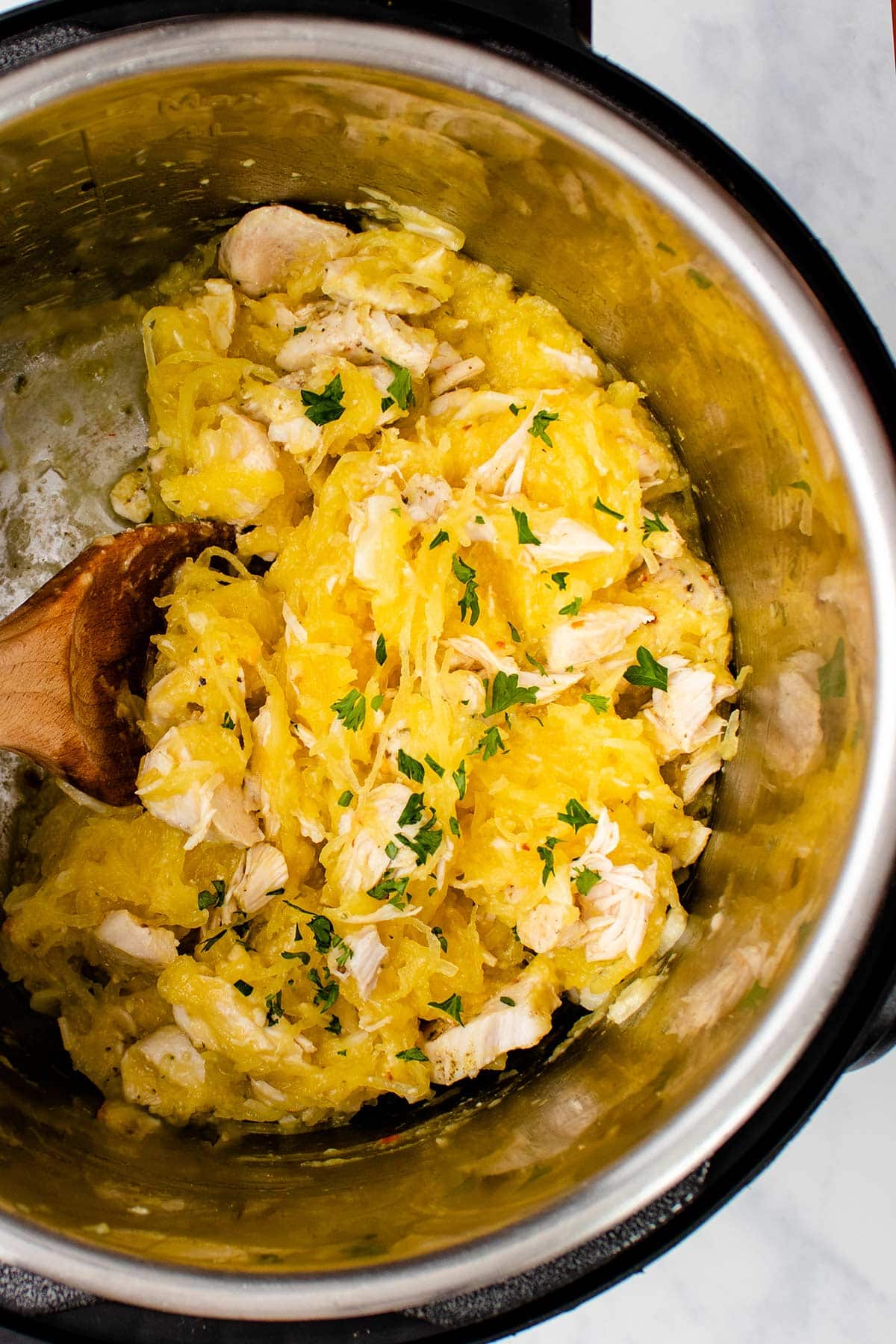 Spaghetti squash with chicken in an Instant Pot with a wooden spoon.