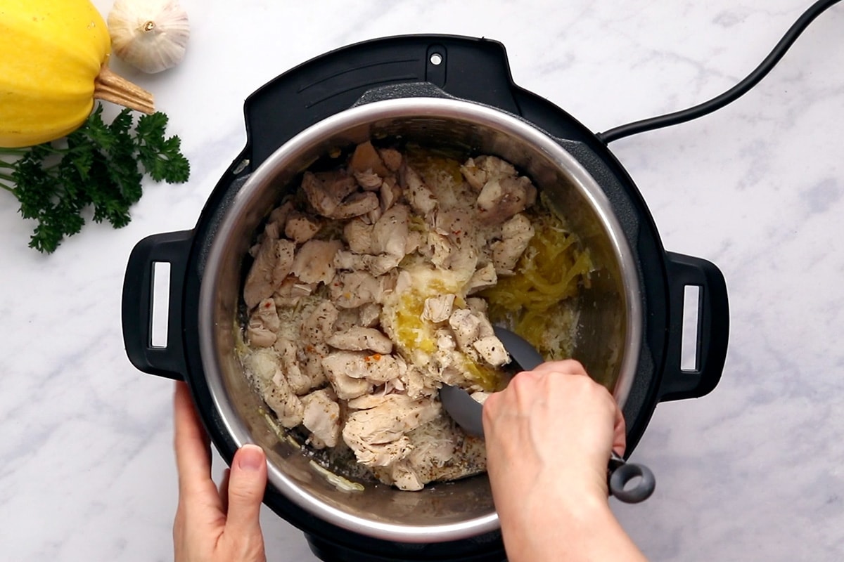 Using tongs to toss chicken breast and parmesan with spaghetti squash in an Instant Pot.