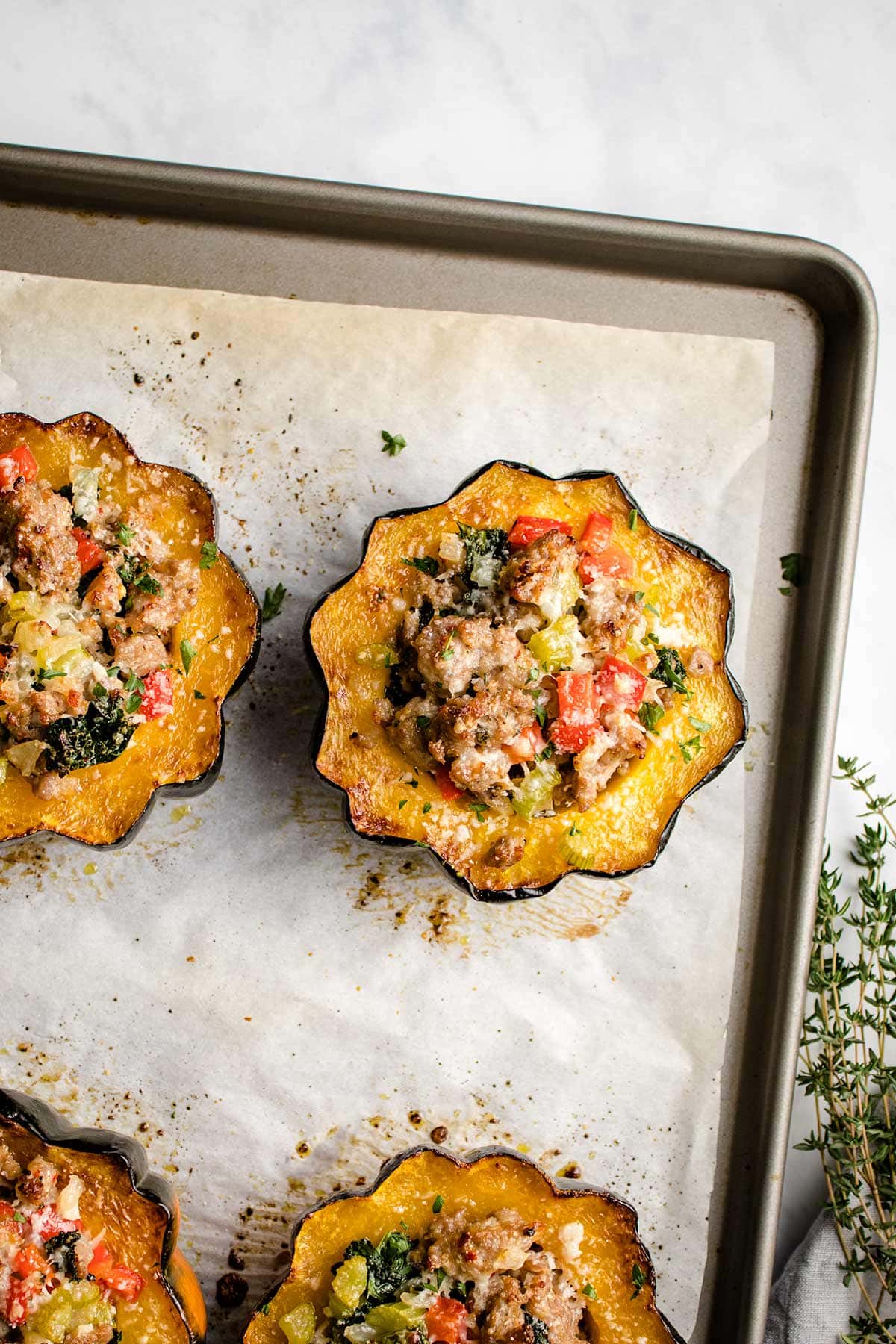 Sausage stuffed acorn squash on a parchment-lined baking tray viewed from overhead.