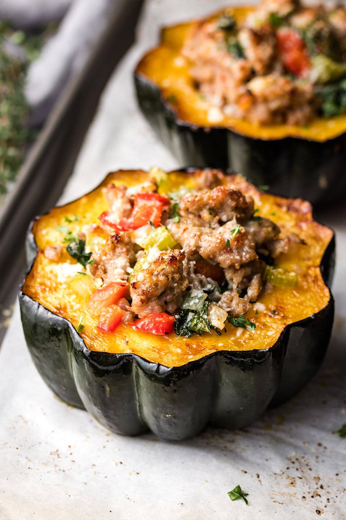 Sausage stuffed acorn squash on a parchment-lined baking tray.