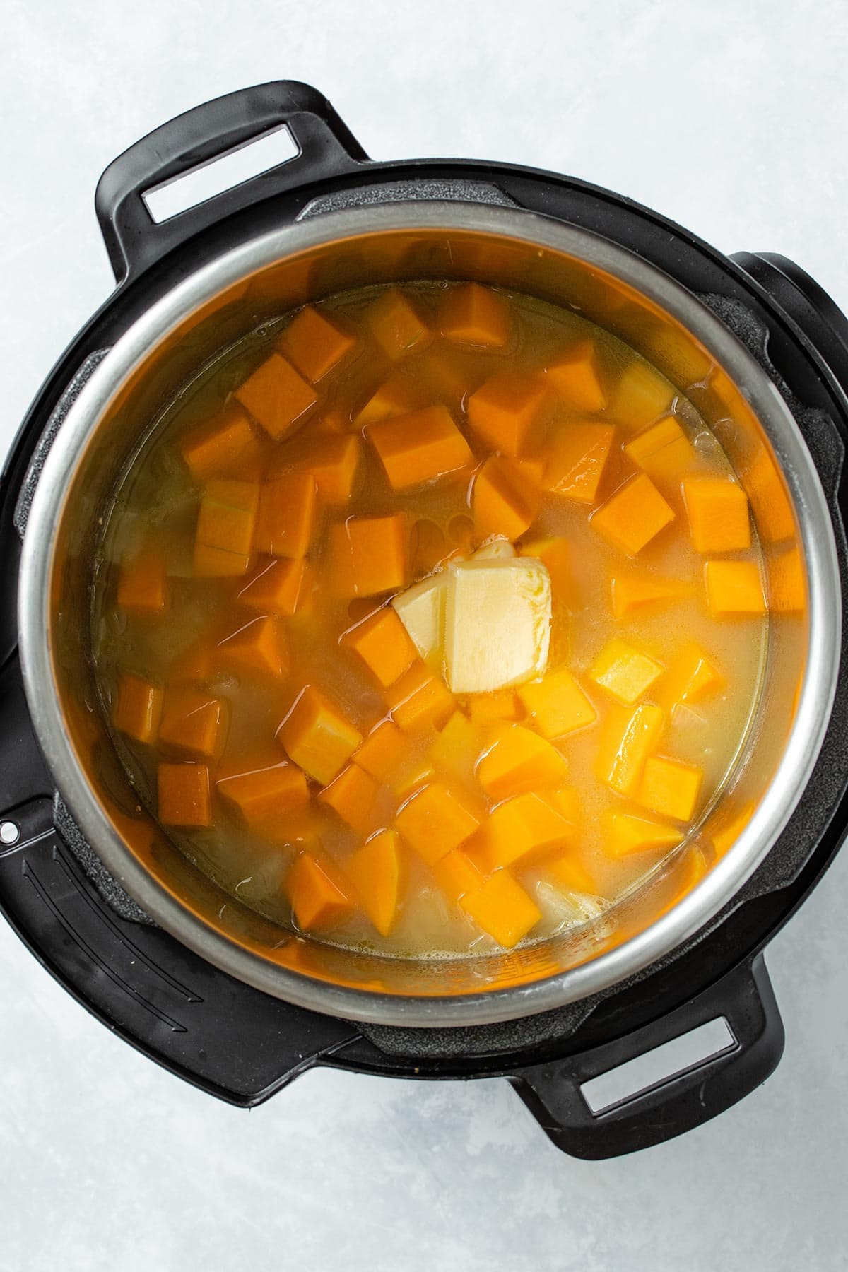 Uncooked diced butternut squash, arborio rice, butter and broth in an Instant Pot viewed from overhead.