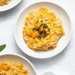 Three white plates filled with butternut squash risotto garnished with crispy sage.