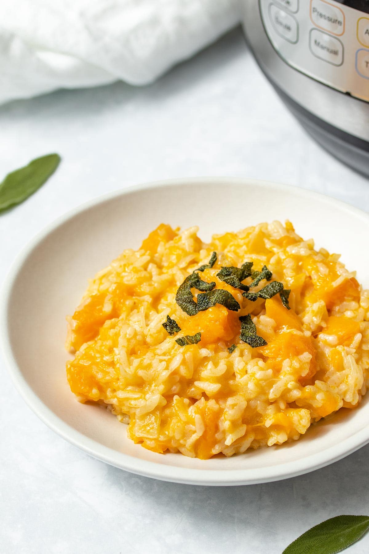 Butternut squash risotto garnished with crispy sage on a white plate with an Instant Pot in the background.