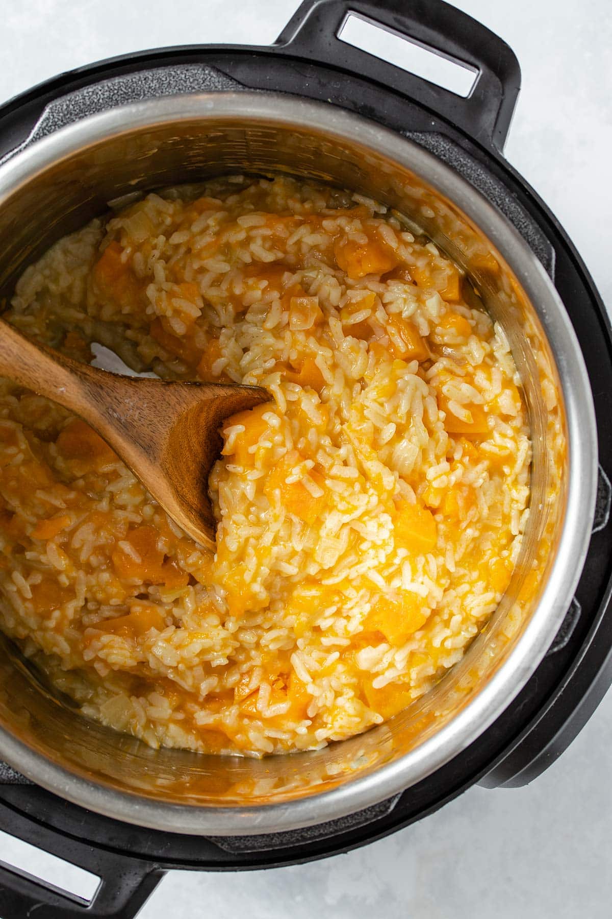 Butternut squash risotto being stirred with a wooden spoon in an Instant Pot.