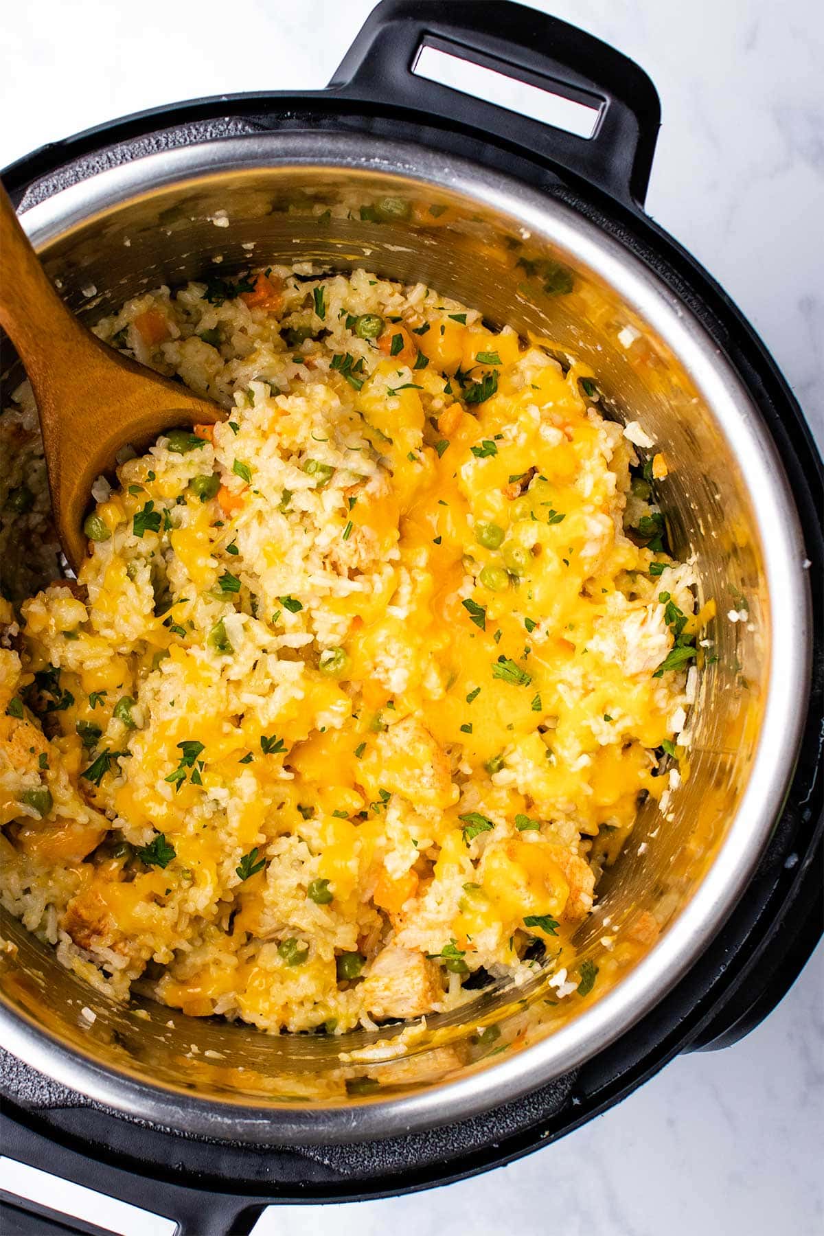 Cheesy chicken and rice in an Instant Pot being scooped by a wooden spoon.