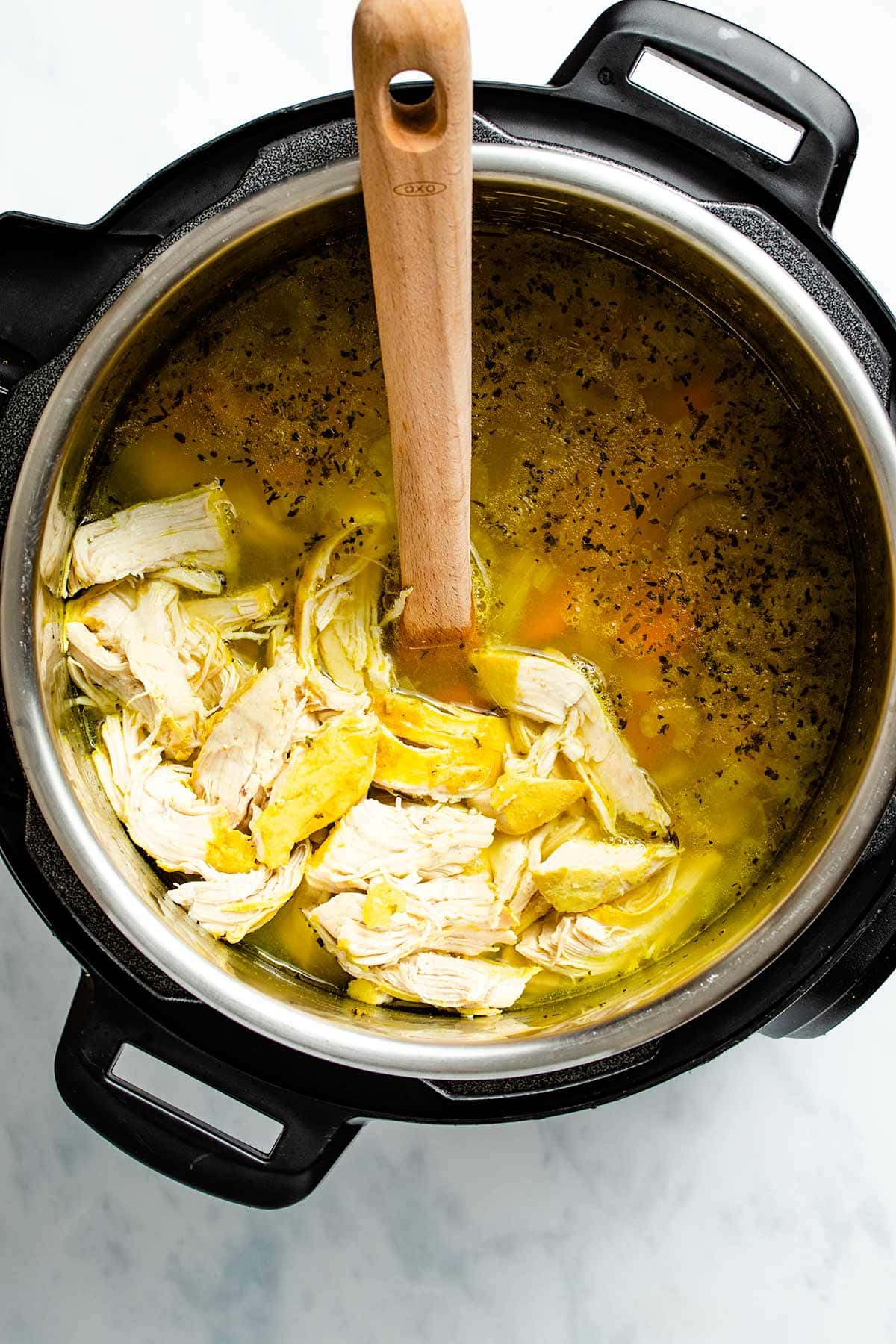 Adding pieces of cooked chicken back to the soup in the Instant Pot.