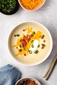 Instant Pot Loaded Cauliflower Soup in a white bowl next to garnishes and a blue linen.