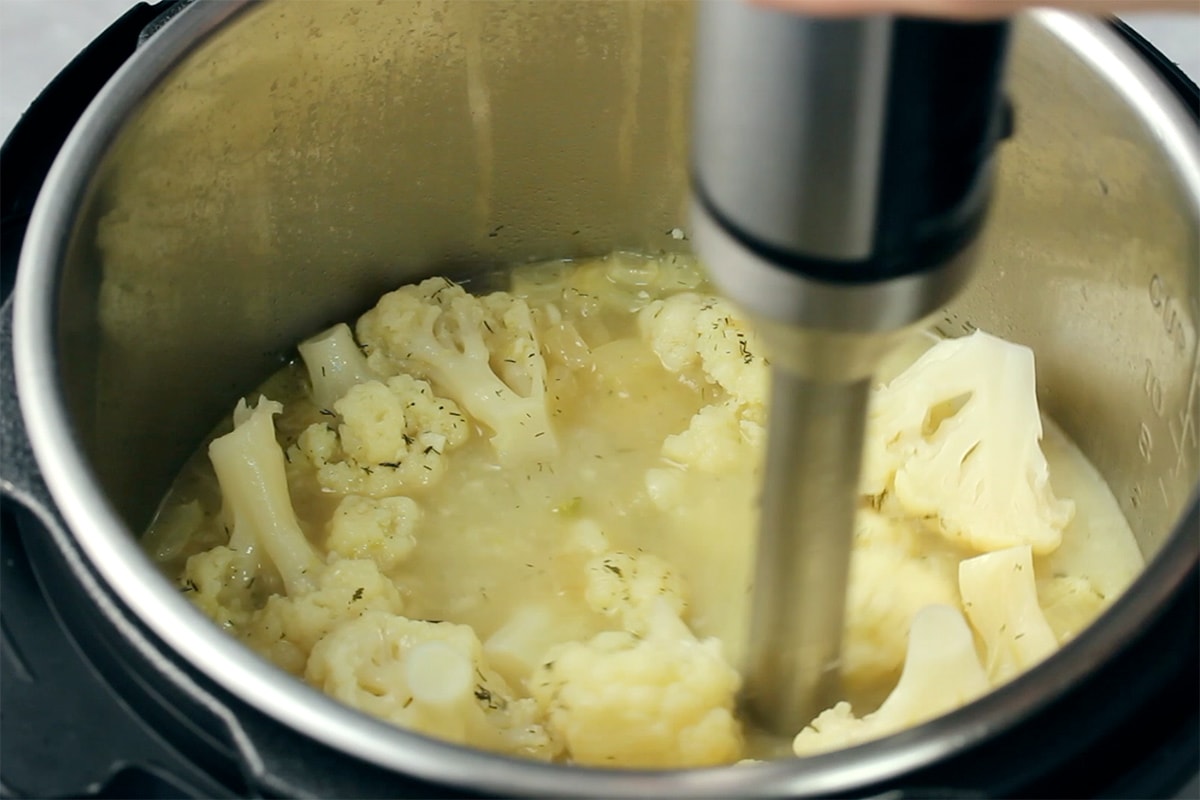 Cauliflower soup being blended with an immersion blender in an Instant Pot.