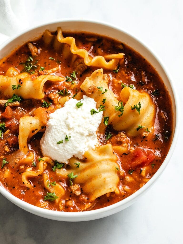 Lasagna Soup in a white bowl garnished with parsley and ricotta cheese.
