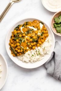 Chickpea spinach curry with a side of rice on a white plate garnished with chopped cilantro.