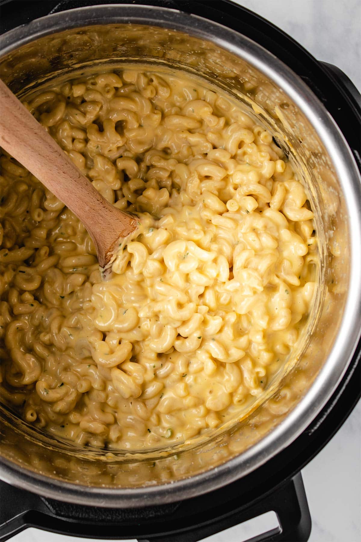 Macaroni and cheese in an Instant Pot being scooped with a wooden spoon.