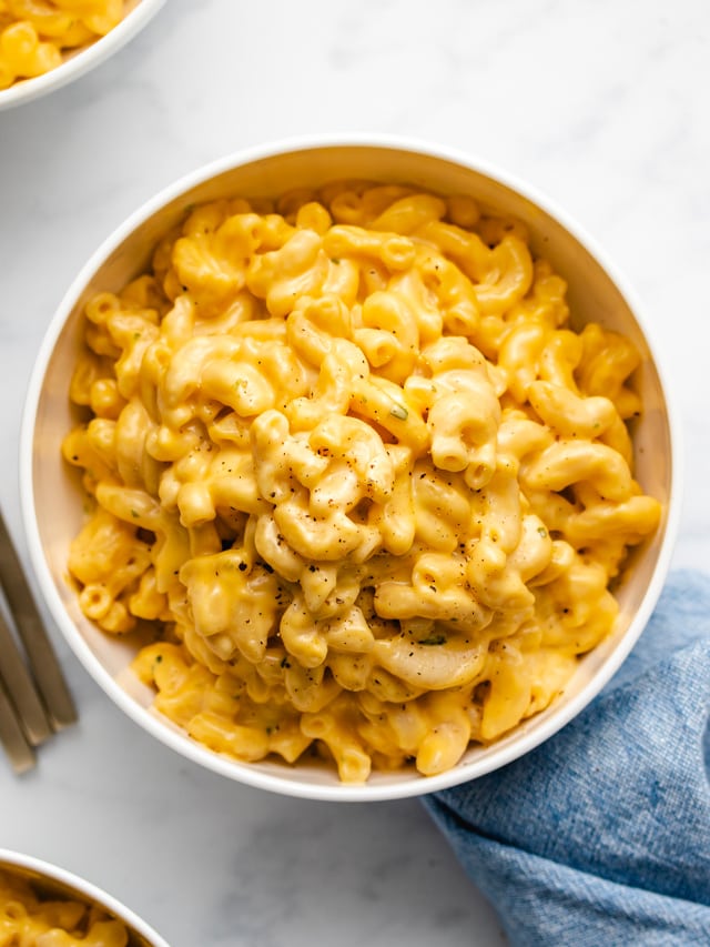 Macaroni and cheese in a white bowl next to a blue linen.