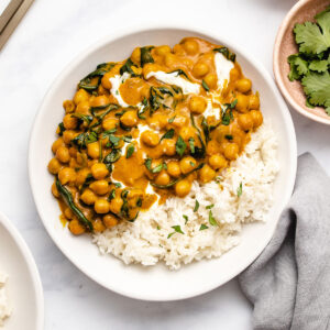 Chickpea Spinach Curry on a white plate served with rice, garnished with yogurt and cilantro.