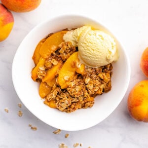 Gluten-free peach crisp in a white bowl topped with ice cream.