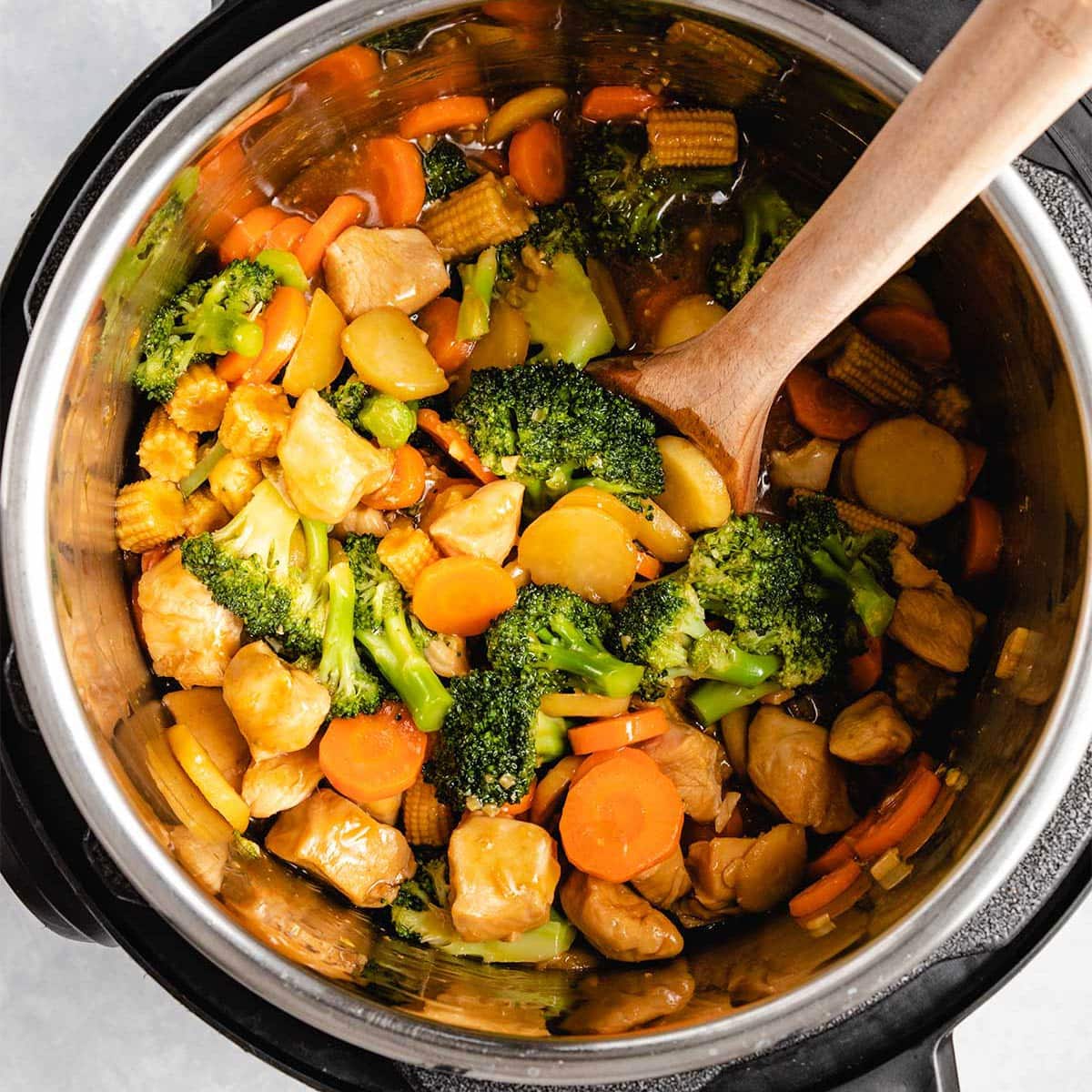 Chicken Stir Fry in an Instant Pot being stirred by a wooden spoon.
