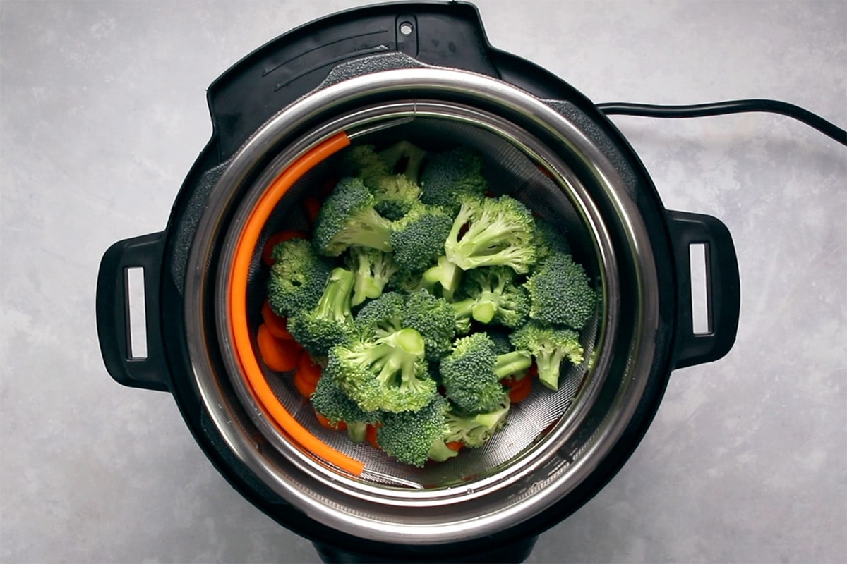 Broccoli florets and sliced carrot in a steamer basket in an Instant Pot viewed from overhead.