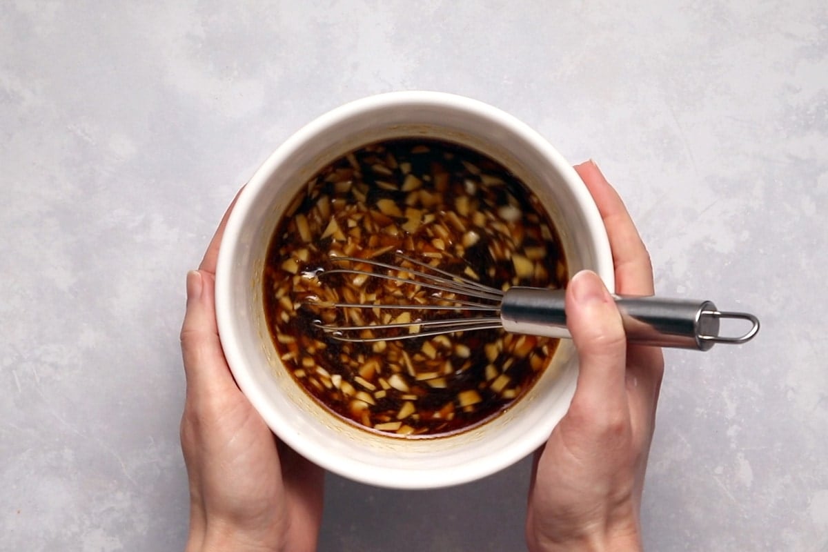 Stir fry sauce with a whisk in a white bowl being held by two hands.