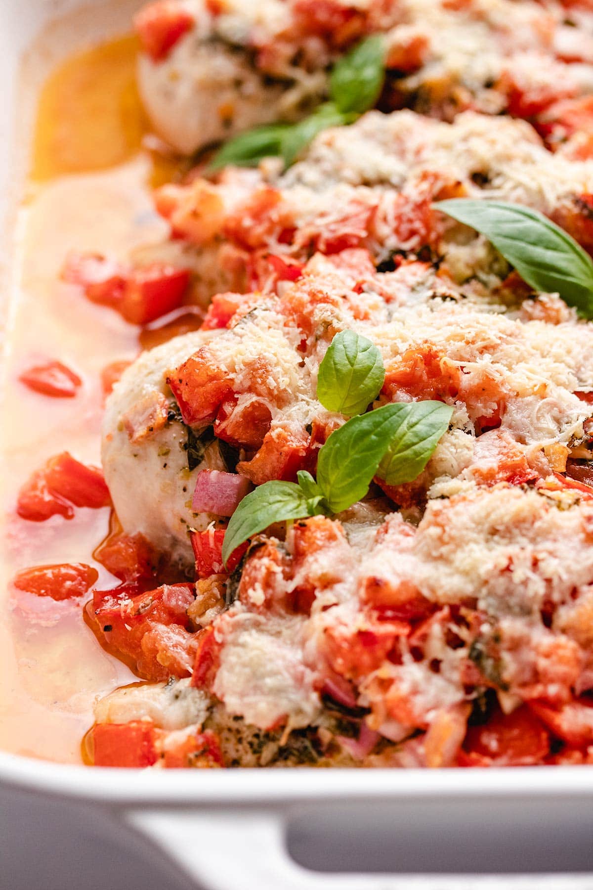 A closeup of bruschetta chicken garnished with basil leaves in a white casserole dish.