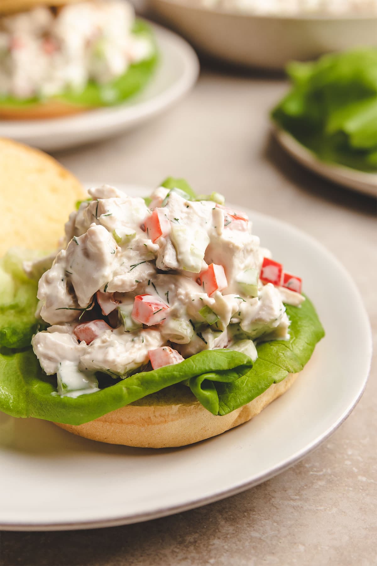 Chicken salad served open face on a brioche bun with lettuce, on a white plate.