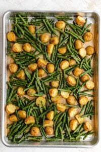 Roasted potatoes and green beans on a parchment-lined baking sheet, viewed from overhead.