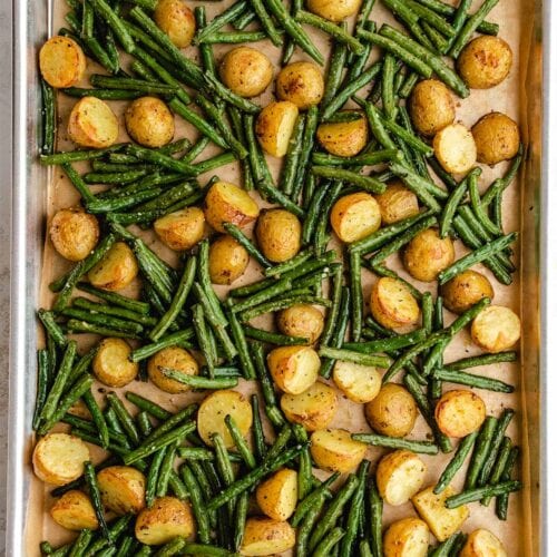 Roasted potatoes and green beans on a parchment-lined baking sheet, viewed from overhead.