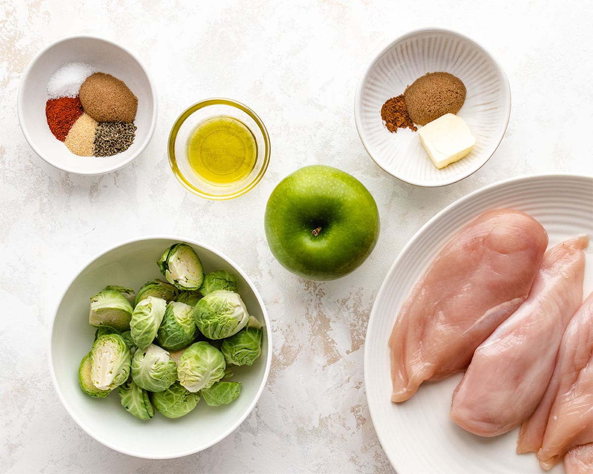 Ingredients needed to make sheet pan chicken, apples and Brussels sprouts, viewed from overhead.