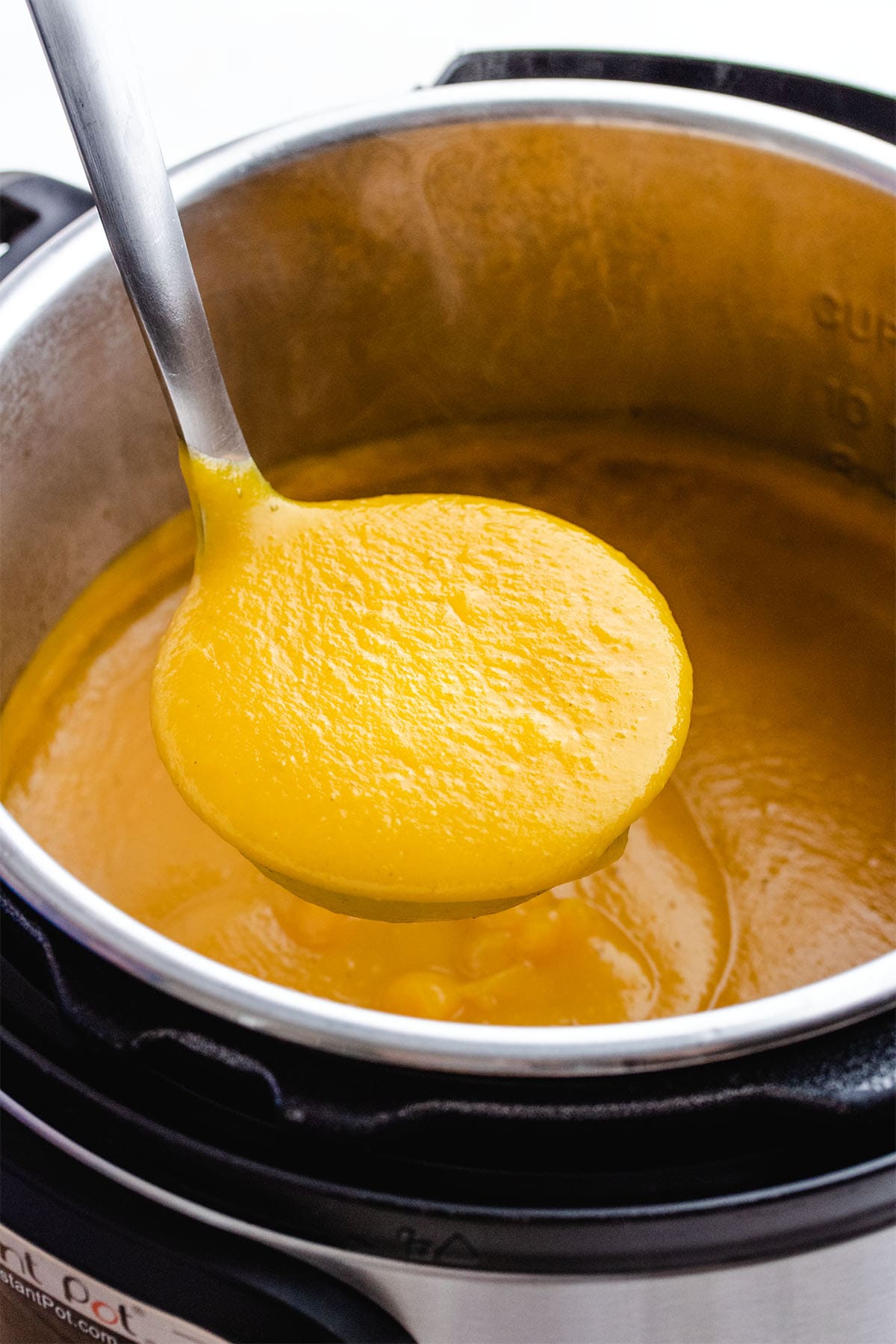 A ladle of butternut squash soup being lifted out of an Instant Pot.
