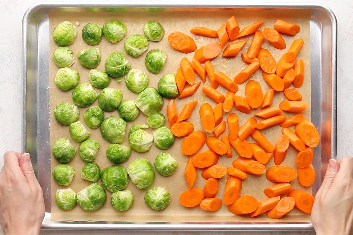 Uncooked Brussels sprouts and carrots on a parchment-lined baking sheet.