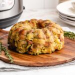 Bundt pan stuffing on a decorative round wooden board, placed in front of an Instant Pot.