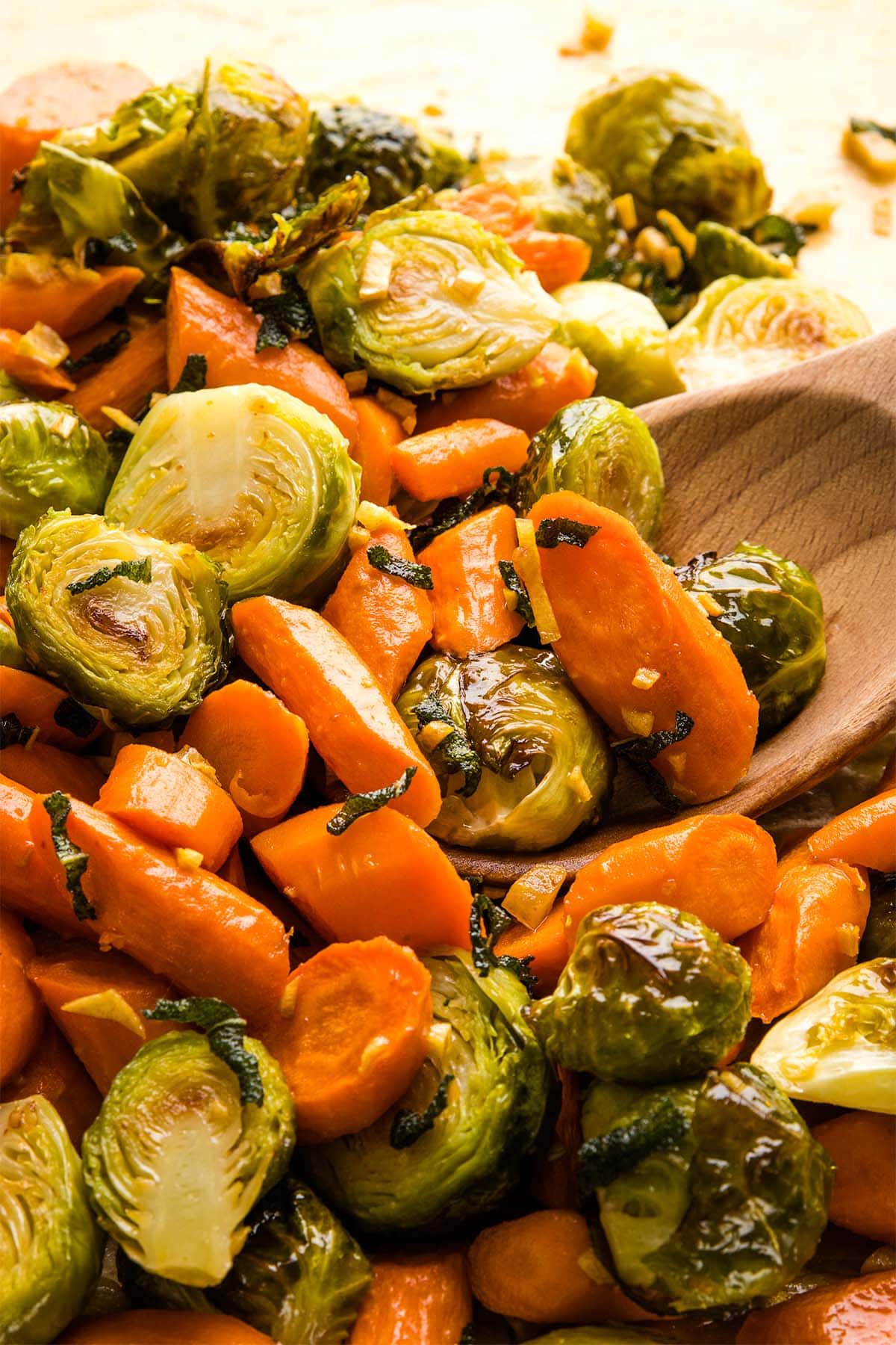 Roasted Brussels sprouts and carrots tossed with brown butter garlic and sage, being scooped by a wooden spoon.