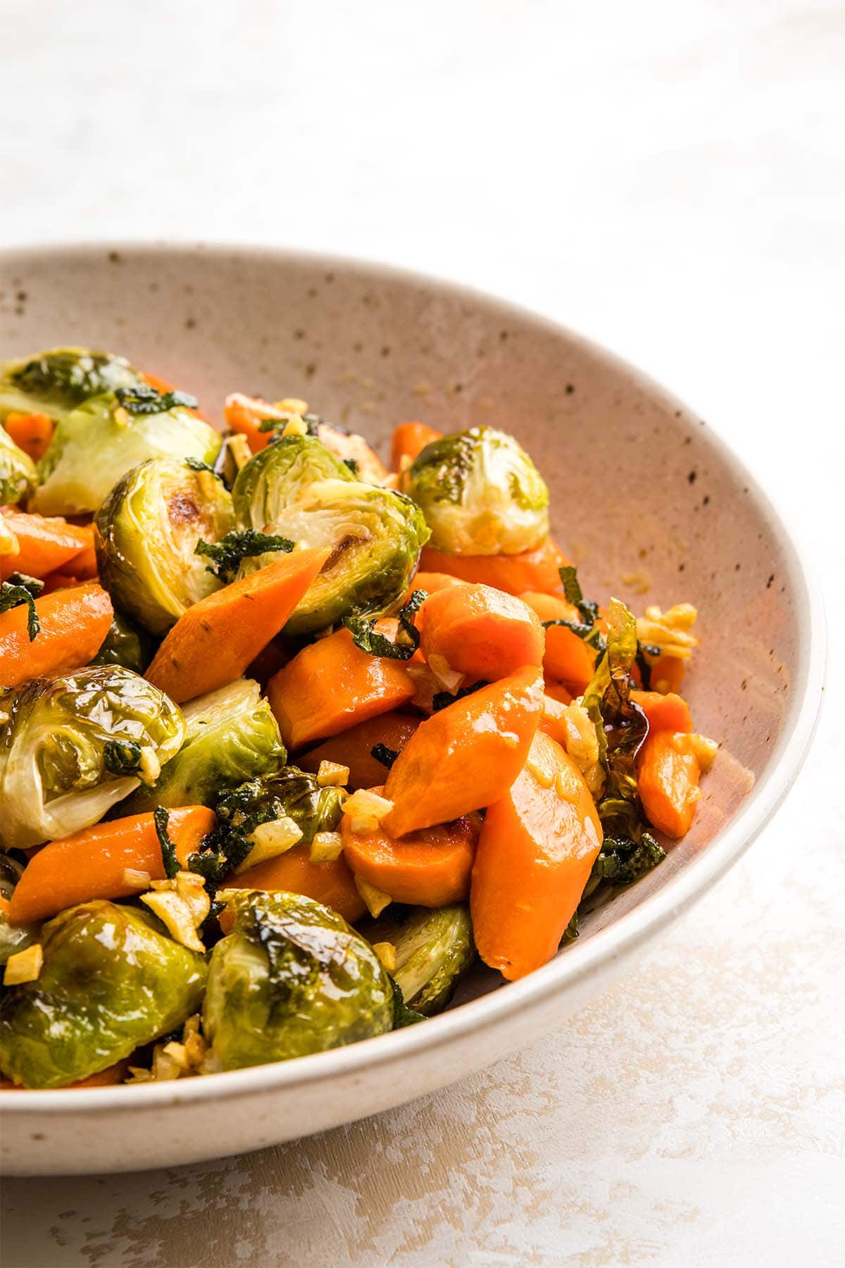 Roasted Brussels sprouts and carrots tossed with brown butter sage in a beige speckled bowl.