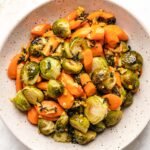 Brown butter sage Roasted Brussels Sprouts and Carrots in a beige speckled bowl, viewed from overhead.