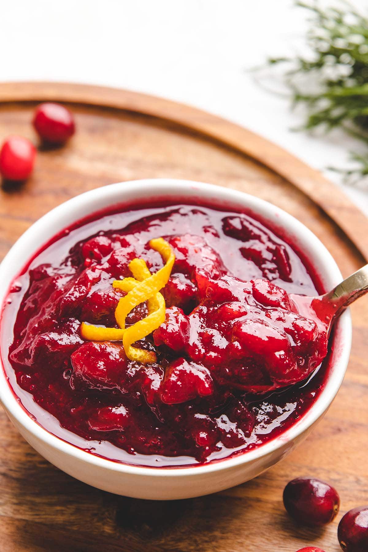 A spoonful of cranberry sauce being taken from a bowlful, garnished with orange peel curls.
