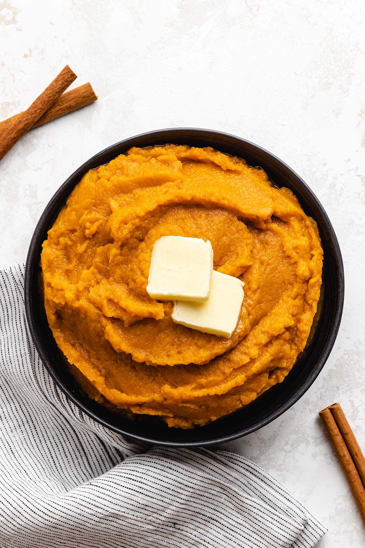 Cinnamon brown sugar mashed sweet potatoes in a black bowl, garnished with butter.