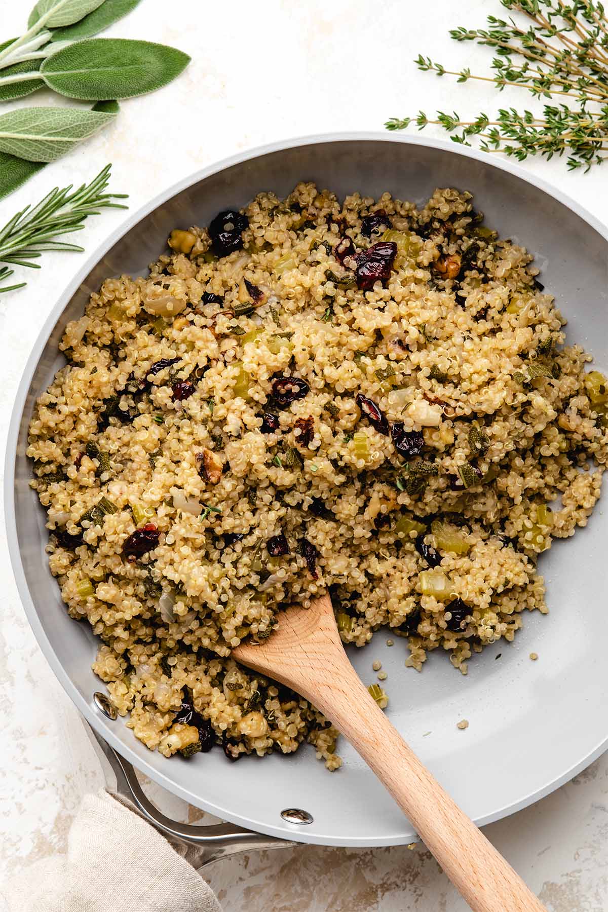 Herbed quinoa stuffing in a light grey skillet, being scooped with a wooden spoon.