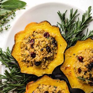 Vegan Stuffed Acorn Squash with herbed quinoa filling on a white serving platter surrounded by fresh herbs.