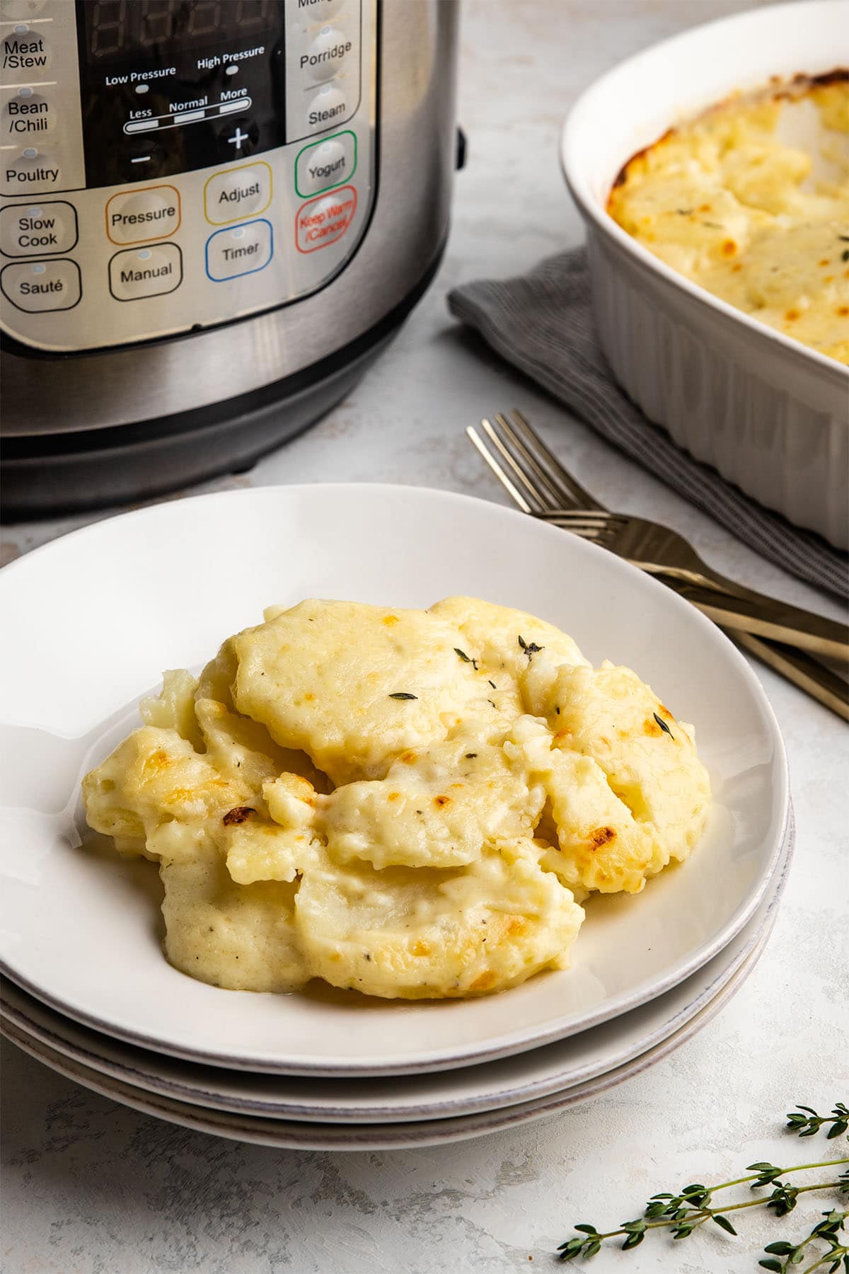 A serving of scalloped potatoes on a stack of white plates, in front of an Instant Pot and the casserole dish.