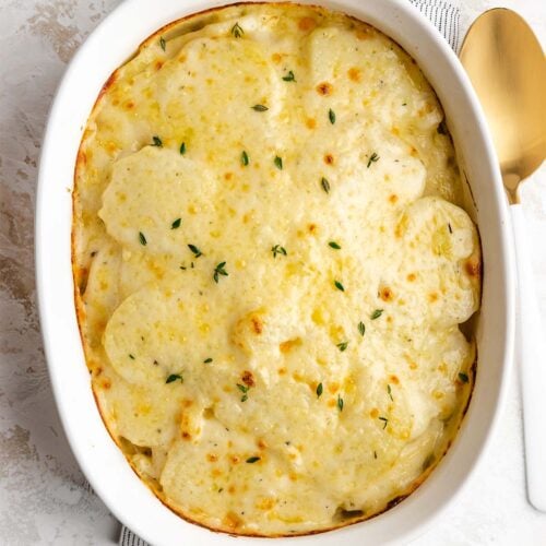 Instant Pot Scalloped Potatoes in a white casserole dish, next to a gold and white serving spoon, viewed from overhead.