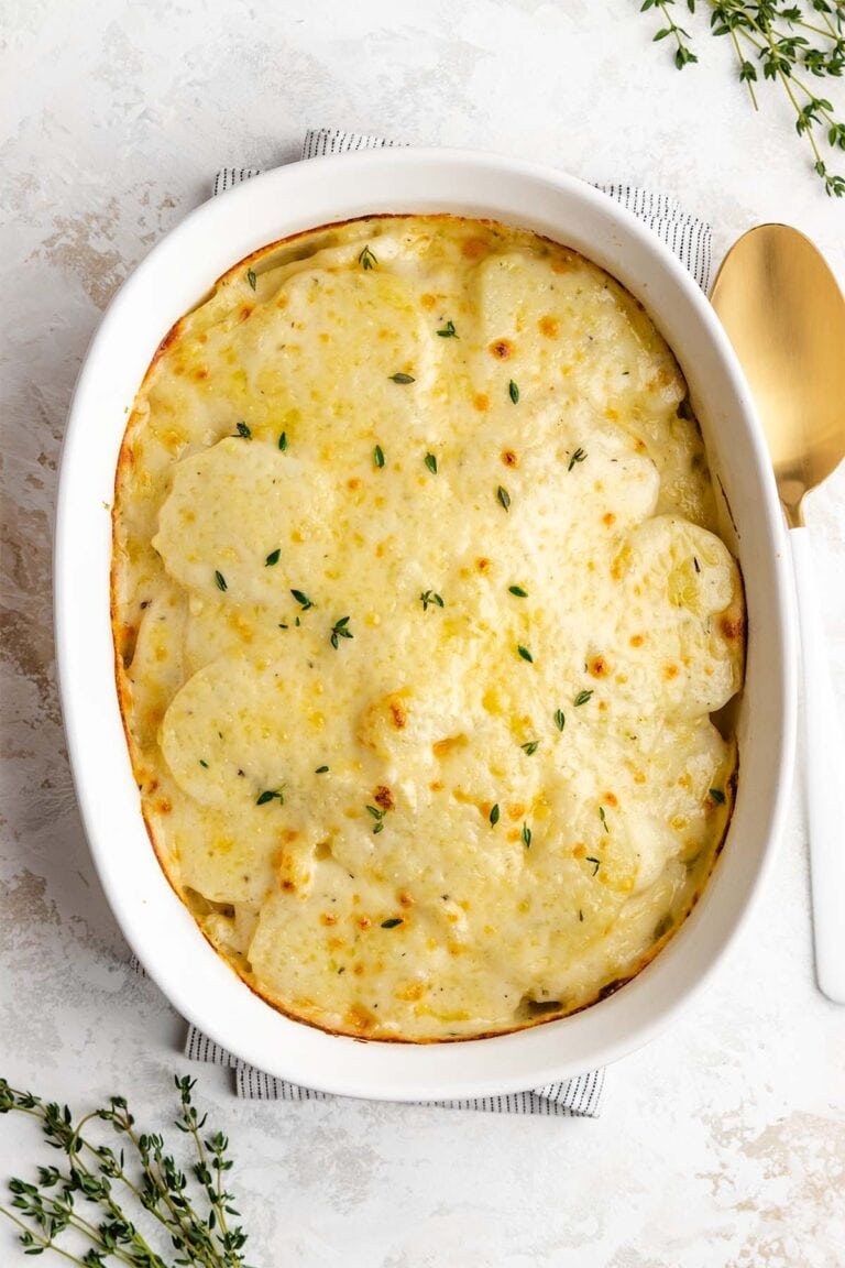 Instant Pot Scalloped Potatoes in a white casserole dish, next to a gold and white serving spoon, viewed from overhead.