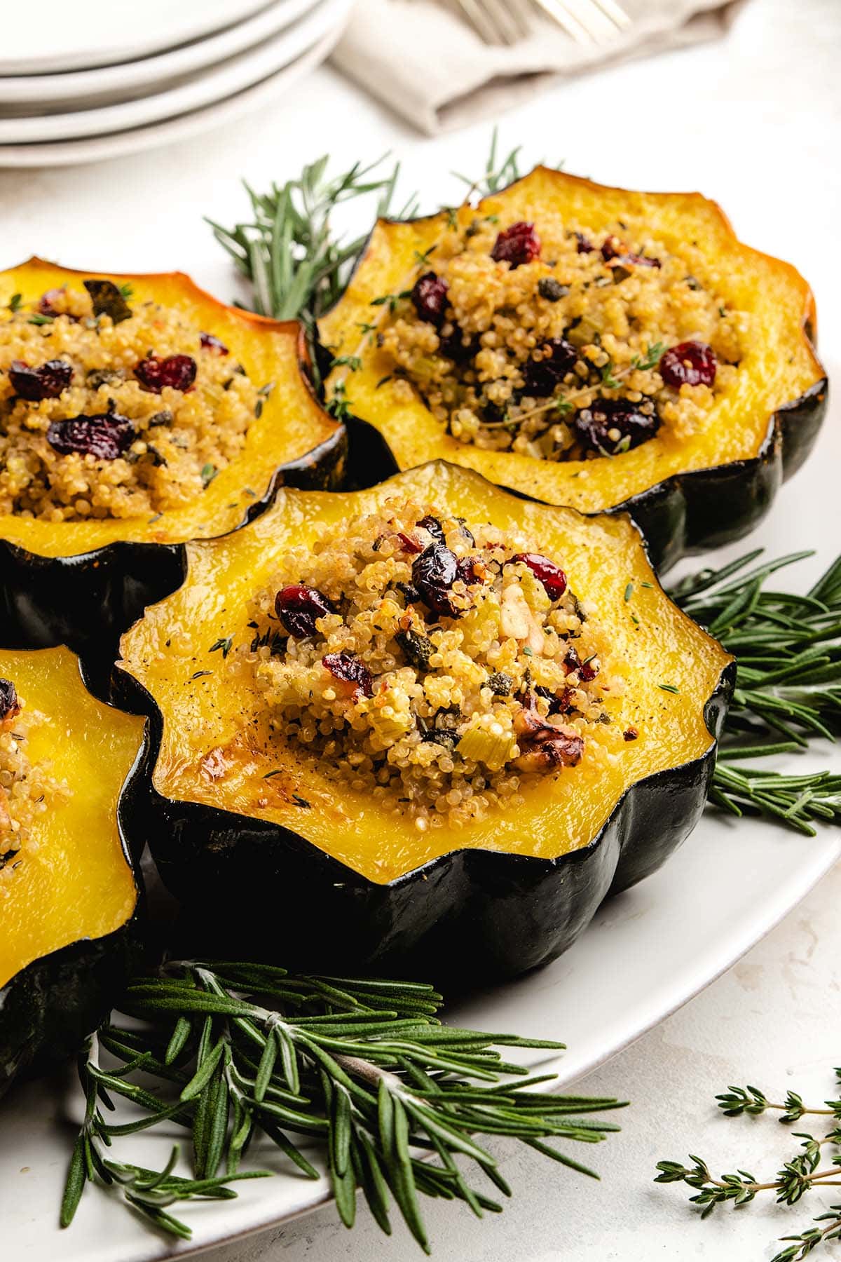 Quinoa Stuffed Acorn Squash on a white serving tray surrounded by fresh herbs.