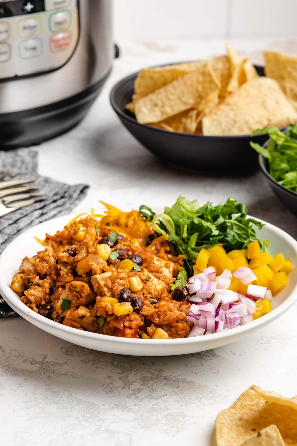 Instant Pot Chicken Burrito Bowl served with diced red onion, yellow bell pepper, shredded lettuce and cheese in a shallow white bowl.