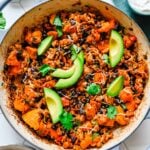 Ground Turkey and Sweet Potato Skillet viewed from overhead in a light blue dutch oven, garnished with cilantro and avocado slices.