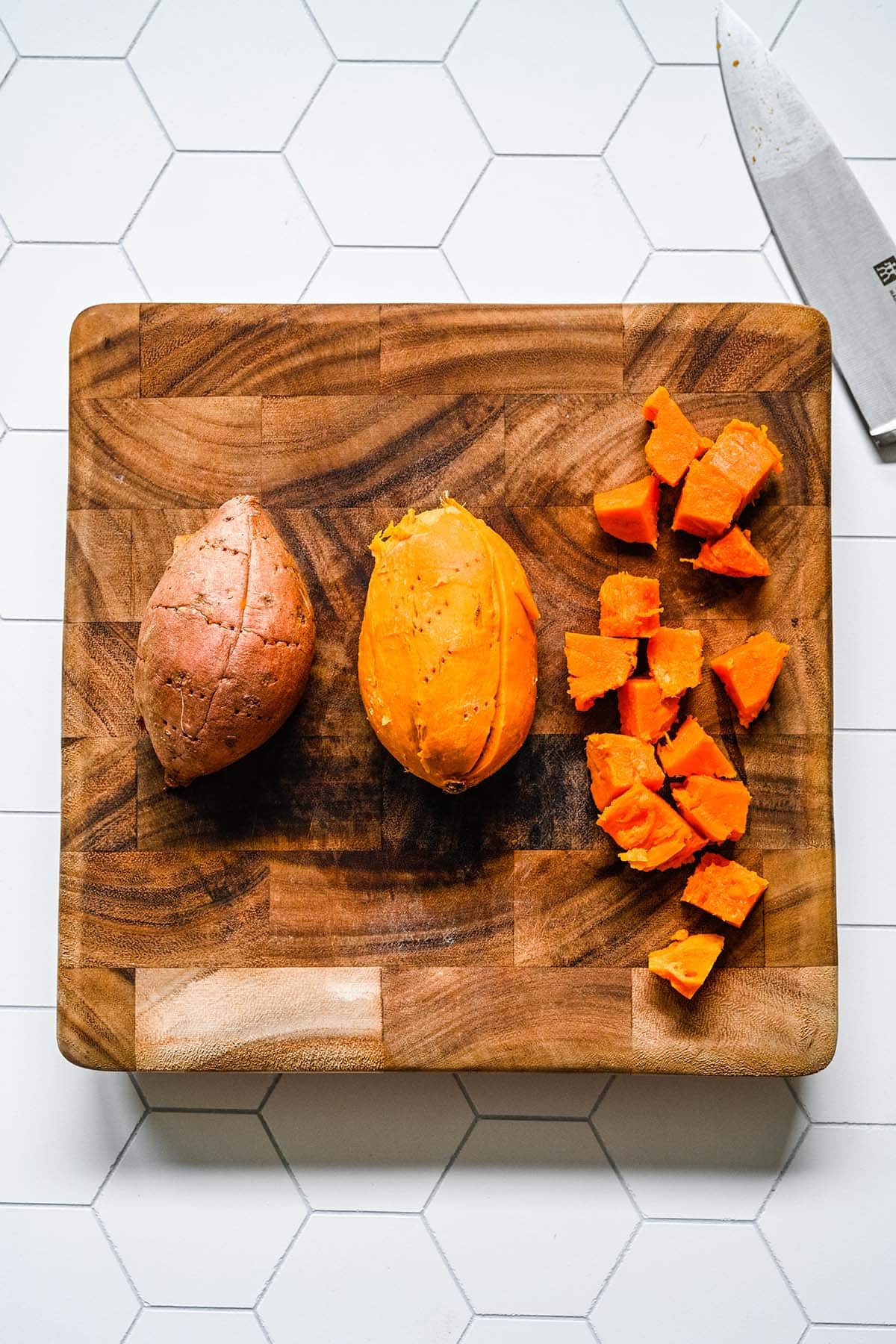 Microwaved sweet potatoes being chopped on a wooden block cutting board.