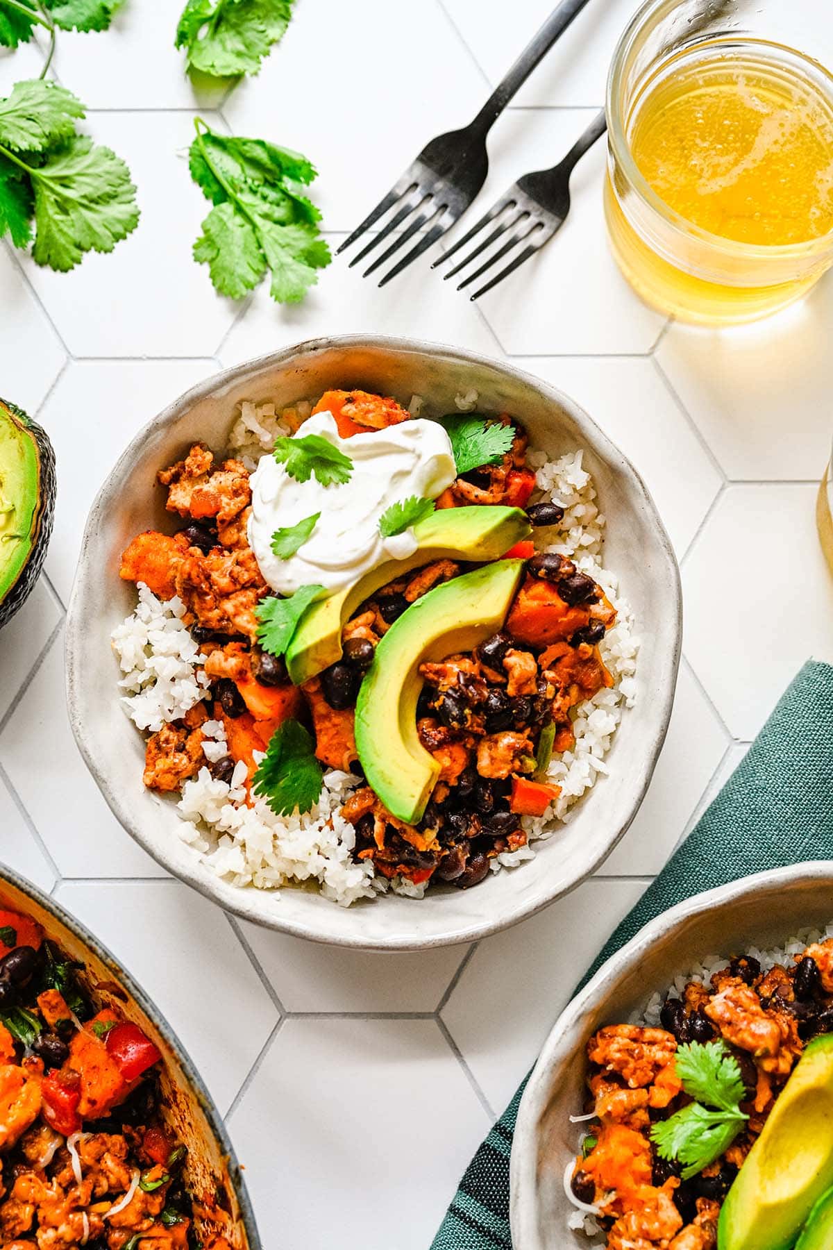 Ground Turkey and Sweet Potato Skillet served over rice in a white bowl, garnished with sour cream, cilantro and sliced avocado.