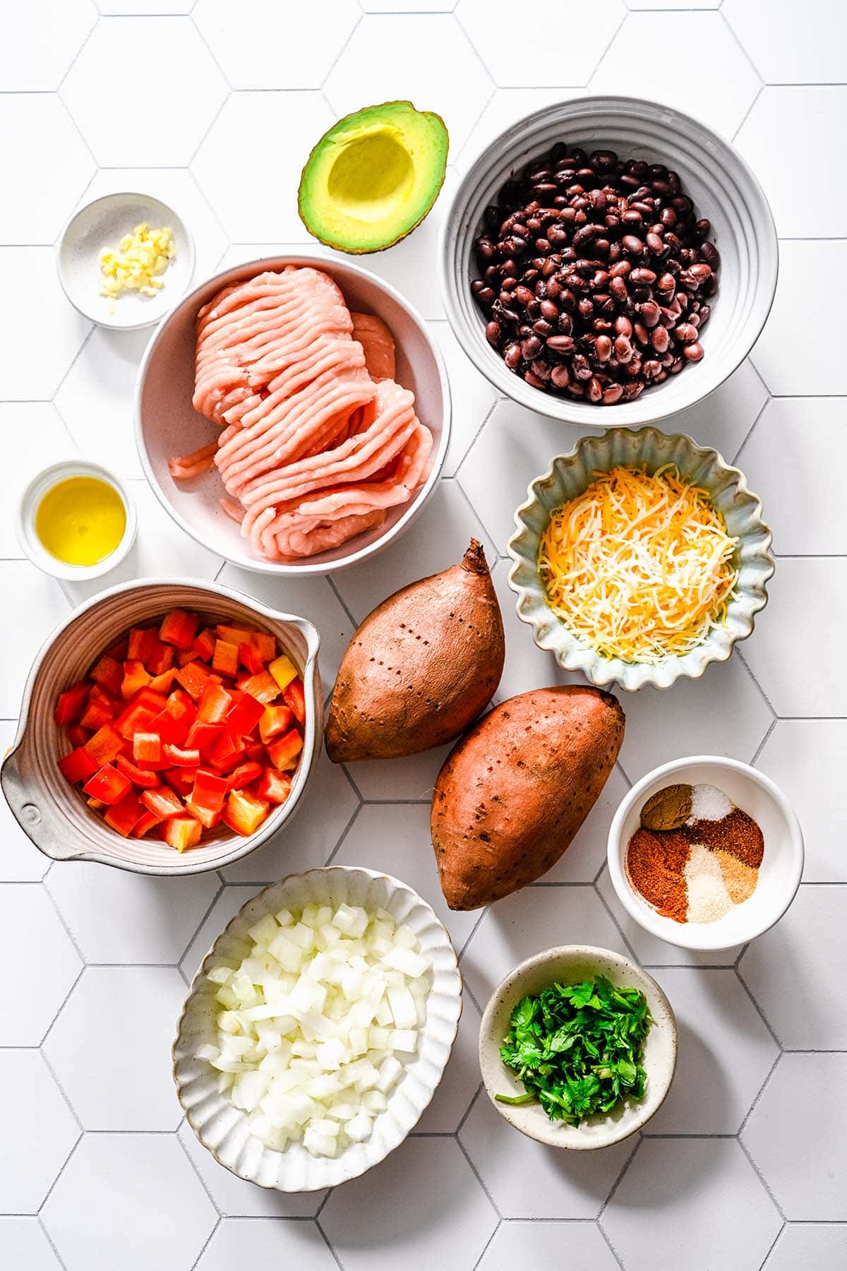 Ingredients needed to make Ground Turkey and Sweet Potato skillet, viewed from overhead on a white hexagon tile background.