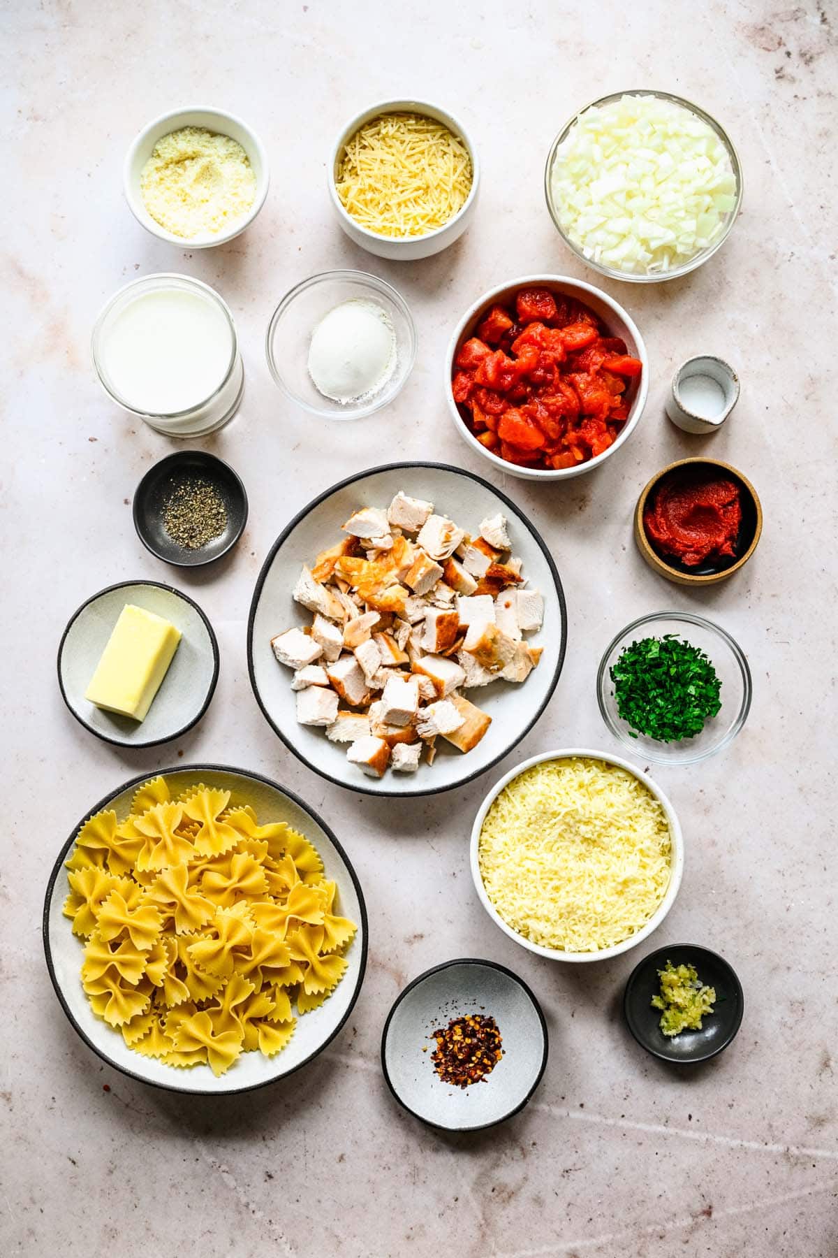 Ingredients needed to make a baked chicken and pasta casserole, arranged in assorted prep bowls, viewed from overhead.