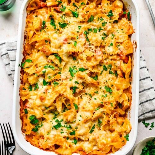 A cheesy chicken pasta bake photographed from above in a white rectangular casserole dish, garnished with chopped fresh parsley.