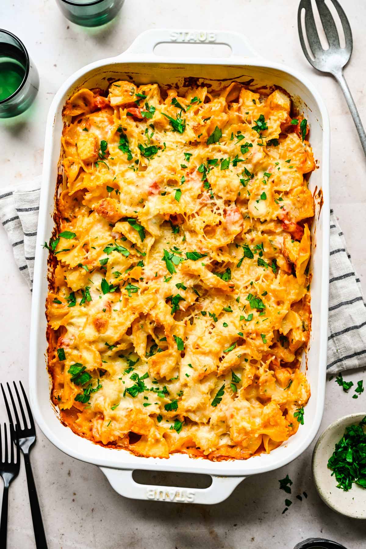 A cheesy chicken pasta bake photographed from above in a white rectangular casserole dish, garnished with chopped fresh parsley.